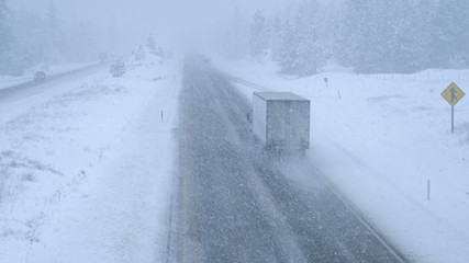 Trucks and cars make their way through a blizzard along a dangerous country road
