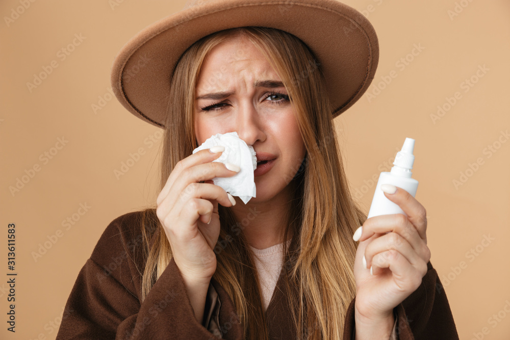 Wall mural image of ill caucasian girl holding nose drops and paper napkin