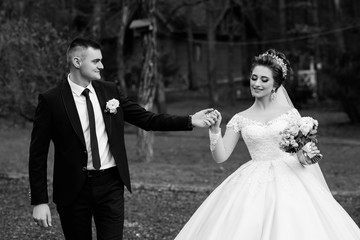 A young and beautiful bride and her husband is standing in park with bouquet of flowers. Amazing smiling wedding couple Beautiful bride and groom on their wedding day. Loving wedding couple outdoor. 