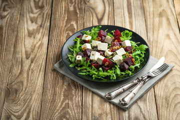 Salad with beetroot, feta cheese, arugula and spicy dressing on a rustic background. Healthy food. Top view. Copy space.