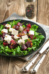 Salad with beetroot, feta cheese, arugula and spicy dressing on a rustic background. Healthy food.