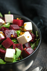 Salad with beetroot, feta cheese, arugula and spicy dressing on a dark background. Healthy food.