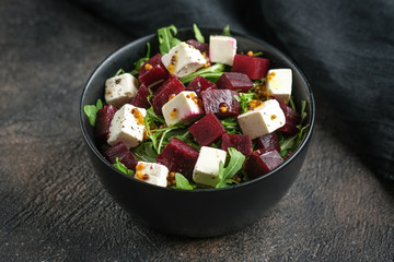 Salad with beetroot, feta cheese, arugula and spicy dressing on a dark background. Healthy food.