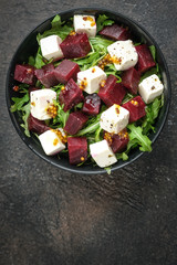 Salad with beetroot, feta cheese, arugula and spicy dressing on a dark background. Healthy food. Top view. Copy space.