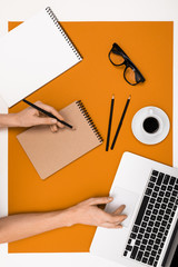 office workplace with notepads with mockup, laptop and pencil on orange surface