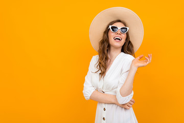 Beautiful caucasian woman in white suit with big hat and sunglasses smiles isolated on orange...