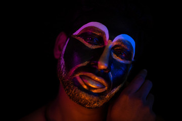 Close up of Indian brunette man with his face illuminated and painted by black and golden like a tribe standing with candle light in front of a black studio copy space background. Indian hi fashion.