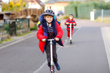 Two little kids boys riding on push scooters on the way to or from school. Schoolboys of 7 years driving through rain puddle. Funny siblings and best friends playing together. Children after school