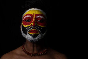 Face of Indian brunette man with his face illuminated and painted by vibrant colors like a tribe standing with candle light in front of a black studio copy space background. Indian hi fashion.