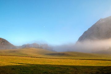 Peaceful foggy landscape with hill above the meadow of horizontal lines under the blue sky