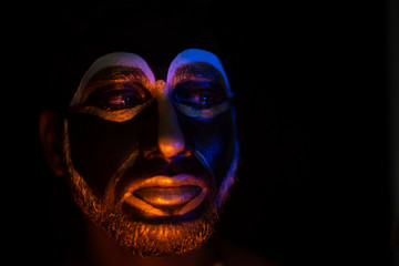 Close up of Indian brunette man with his face illuminated and painted by black and golden like a tribe standing with candle light in front of a black studio copy space background. Indian hi fashion.