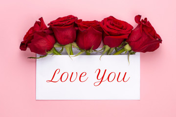 Love you banner. Red rose flowers arrangement with blank card on light pink background.