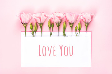 Love you banner. Eustoma flowers arrangement with blank card on light pink background.