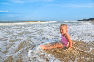 Girl in pink swimsuit sitting on the beach and looking at the morning sea.