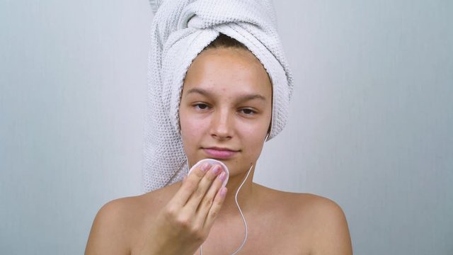 Shirtless teenager with acne cleansing face and listening to music after bath