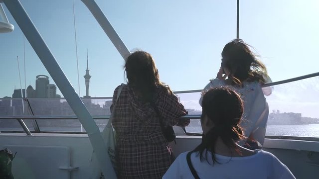 Three female tourists taking photo of Auckland Sky Tower from ferry, New Zealand