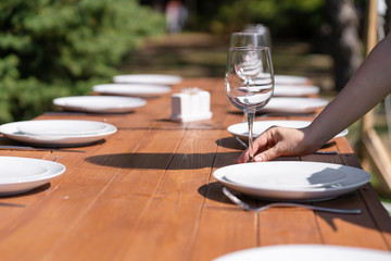 Girl the waiter in a summer cafe under the open sky arranges the dishes on a wooden banquet table.