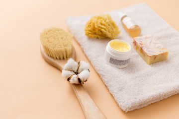 Fototapeta na wymiar beauty, spa and wellness concept - close up of crafted soap bar, natural bristle wooden brush, body butter with sponge and essential oil on bath towel