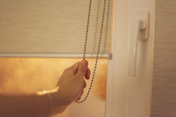 Hand holds the chain and opens the roller blinds on the window, bed shade.