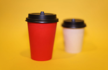 Paper cups and red and white for coffee and cappuccino stand on a yellow background, minimalism.