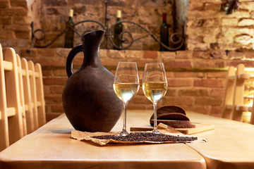 Two glasses of white wine, grape seeds, a clay jug and a few pieces of bread on a wooden table in a restaurant
