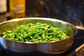 Green beans in a steel pan standing on a ceramic plate on a dark background.