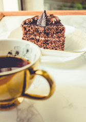 Dark Chocolate cake on a white plate and yellow gold cup of tea. Selective focus. Sweet dessert. Toning