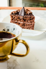 Dark Chocolate cake on a white plate and yellow gold cup of tea. Selective focus. Sweet  birthday dessert.