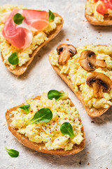 Scramble omelet sandwiches, bacon, mushrooms, tomatoes and fresh herbs on a light gray background.