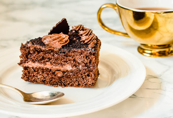 Piece of chocolate cake in a white plate and gold cup of coffee, closeup. Selective focus. Seasonal and holidays pattern