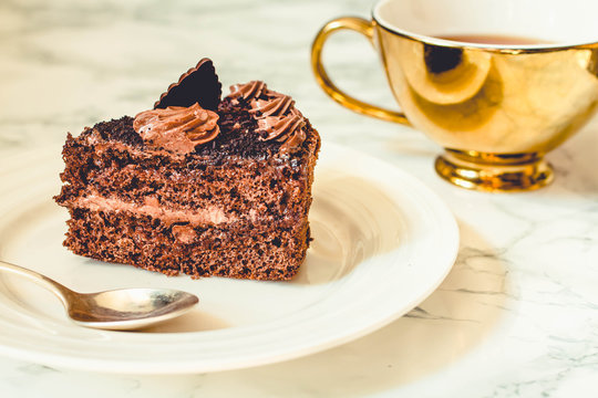 Piece of chocolate cake in a white plate and gold cup of coffee, closeup. Selective focus. Seasonal and holidays pattern. Tone