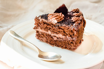 Piece of chocolate cake in a white plate and gold cup of coffee, closeup. Selective focus.