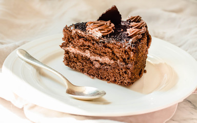 Piece of chocolate cake in a white plate and gold cup of coffee, closeup. Selective focus.