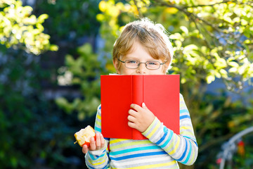 Happy little preschool kid boy with glasses, books, apple and backpack on his first day to school or nursery. Funny healthy child outdoors on warm sunny day, Back to school concept. Laughing boy.