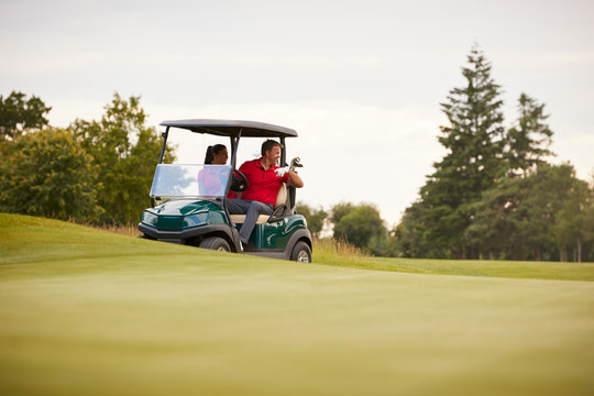 Front View Of Couple Playing Golf Driving Buggy Along Fairway On Red Letter Day