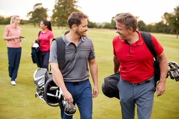 Two Mature Couples Playing Round Of Golf Carrying Golf Bags Along Fairway