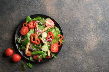 Fresh vegetable salad with chicken meat, herbs and olive oil in a dark plate on a dark background. Healthy food. Top view copy space.