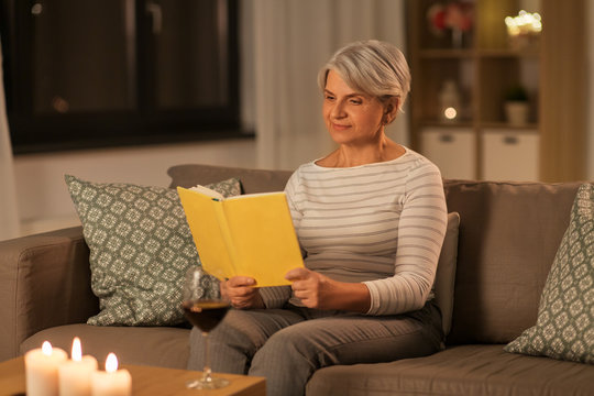 Age, Leisure And People Concept - Happy Senior Woman Reading Book At Home In Evening