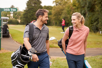 Mature Couple Playing Round Of Golf Carrying Golf Bags And Talking