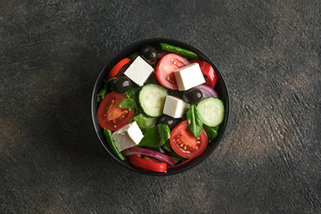 Fresh vegetable salad with feta, olives and herbs in a dark plate on a dark rustic background. Healthy vegan food. Top view copy space.
