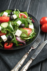 Fresh vegetable salad with feta, olives and herbs in a dark plate on a dark rustic background. Healthy vegan food.
