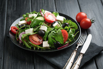 Fresh vegetable salad with feta, olives and herbs in a dark plate on a dark rustic background. Healthy vegan food.