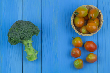 Fresh tomatoes in the basket and .broccoli on the blue wooden table