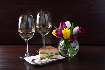 tasty fresh tiramisu cake on a brown background with a bouquet of tulips
