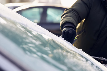 Man scraping ice from the windshield of a car covered wit hoarfrost