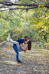 Fototapeta premium Young beautiful couple in the Park. A man holds a woman in his arms. In the background autumn forest.