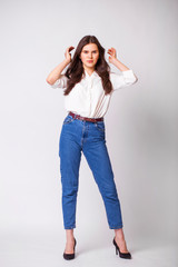 Beautiful brunette woman in blue jeans and white shirt, isolated on gray background