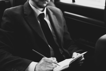 Closeup portrait of a young businessman with a beard. In stylish clothes, sits in the passenger seat, writing information in a notebook. In creative tinting. Business concept business style