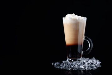 Irish coffee with ice pieces on a black background.