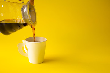 Hand pouring liquid coffee put in the cup on a yellow paper background. Copy space for your text.